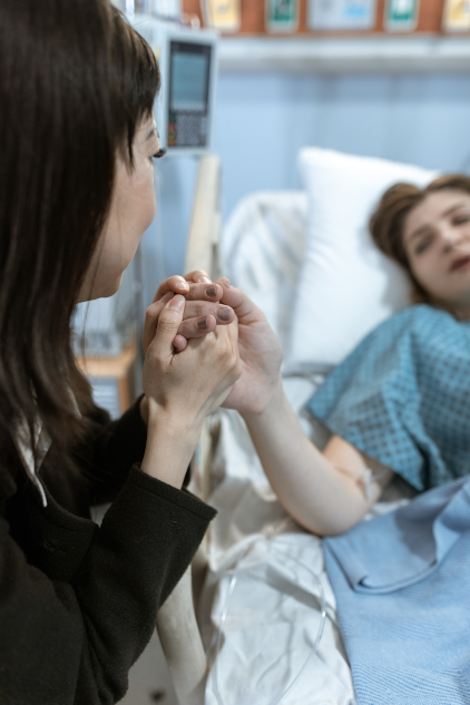 Woman in a hospital bed with friend holding her hand